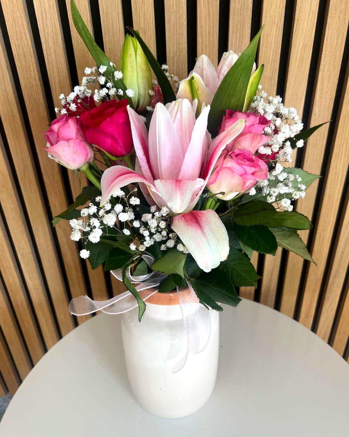 Blumenarrangement mit Lilien, Rosen und Schleierkraut in weisser Vase – TIKIS